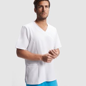 Un hombre viste una Casaca de servicios de manga corta blanca con bolsillos delanteros, de pie sobre un fondo liso gris claro y mirando ligeramente hacia arriba con expresión neutra.