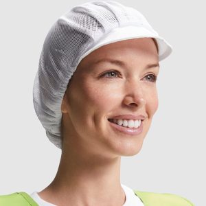 Una persona sonriente lleva una camisa verde claro y la Gorra-Cofia con rejilla y visera corta - Ajuste transpirable, mirando ligeramente hacia la derecha sobre un fondo liso gris claro.