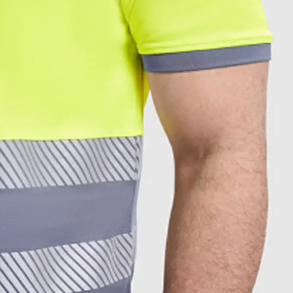 Detalle del brazo y torso de un hombre vistiendo un polo técnico de alta visibilidad en color amarillo neón con cinta reflectante gris y detalles diagonales, sobre fondo claro liso.