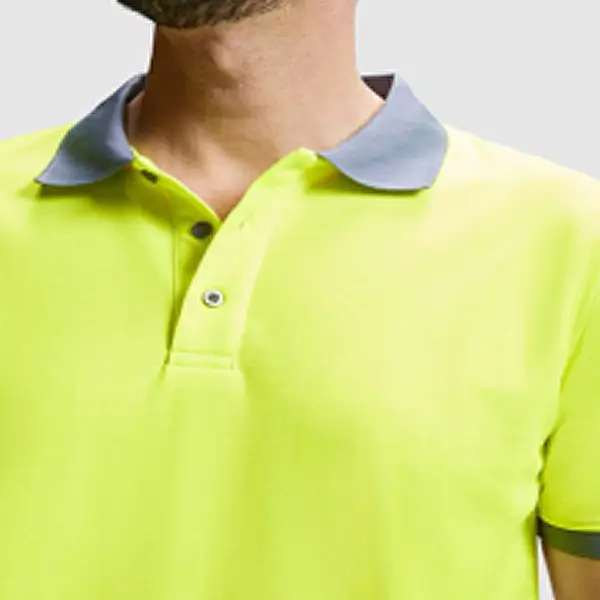 Primer plano del torso de un hombre vistiendo un polo técnico de alta visibilidad en color amarillo neón con cuello gris, sobre fondo claro liso.